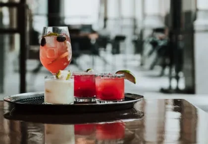 Four colorful drinks on a silver tray in a modern bar.