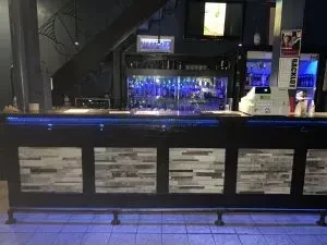 Modern bar interior with dark counter, blue LED lights, and bottles.