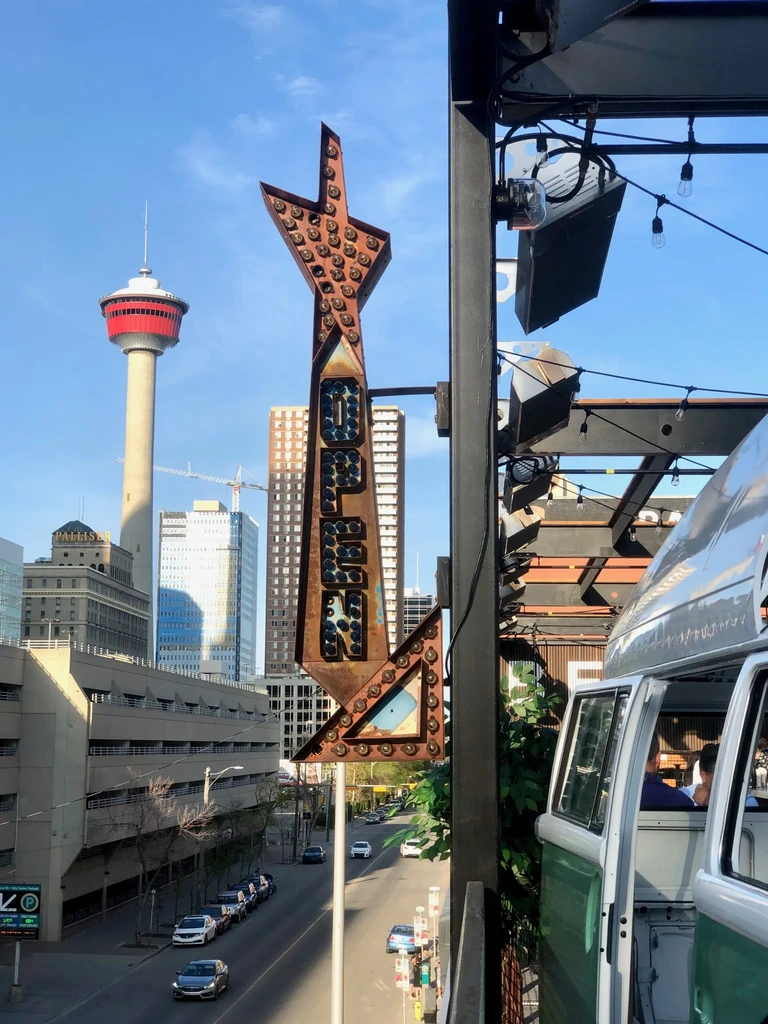 Rooftop patio with 'OPEN' sign, vintage VW bus, and Calgary skyline.