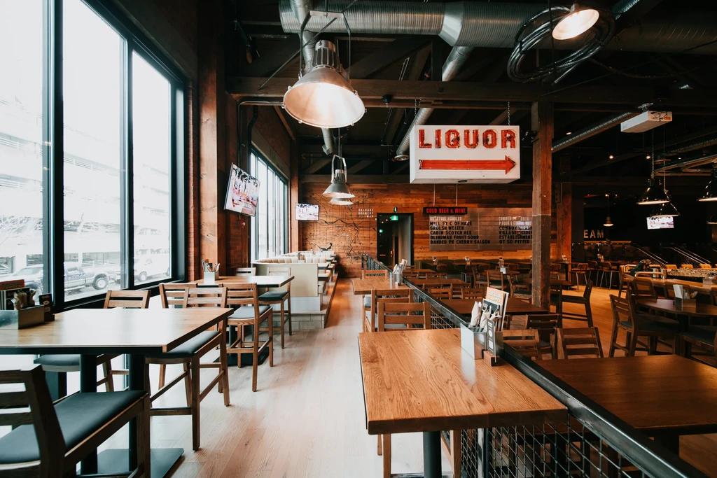 Empty modern-industrial restaurant interior with wooden tables and 'LIQUOR' sign.