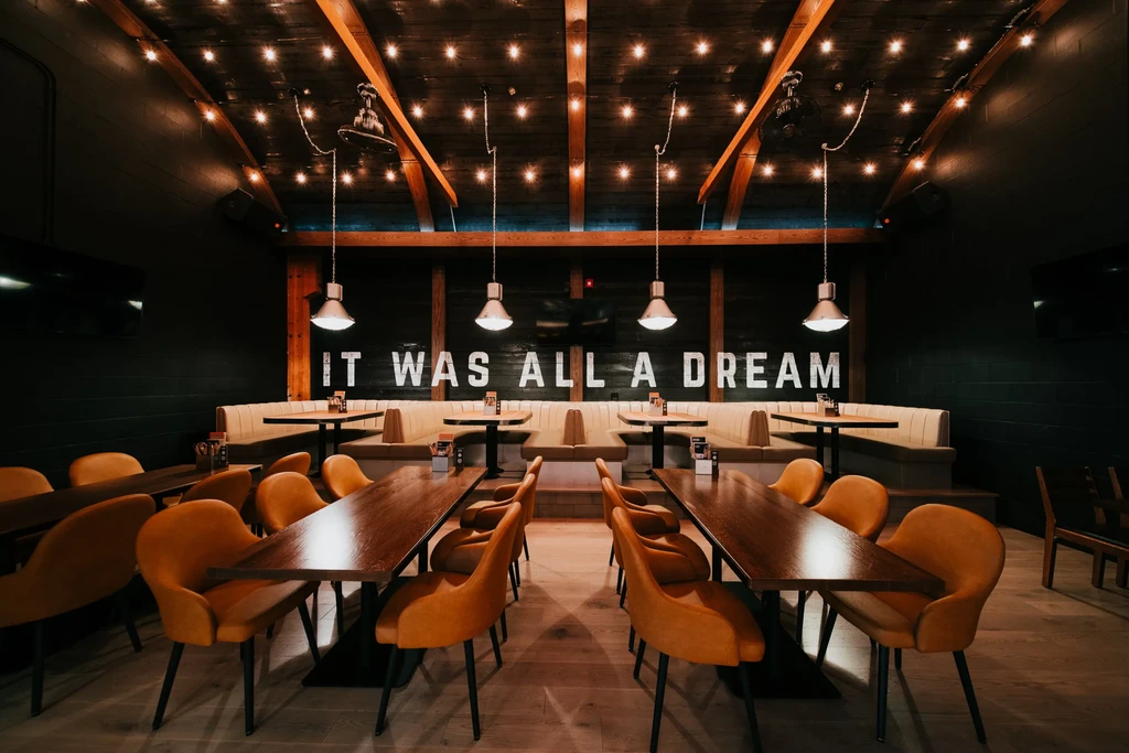 Dark modern restaurant interior with yellow chairs, wooden ceiling, and string lights.