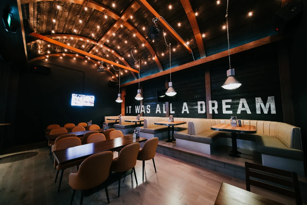 Empty, stylish restaurant interior with vaulted wood ceiling and 'IT WAS ALL A DREAM' text.