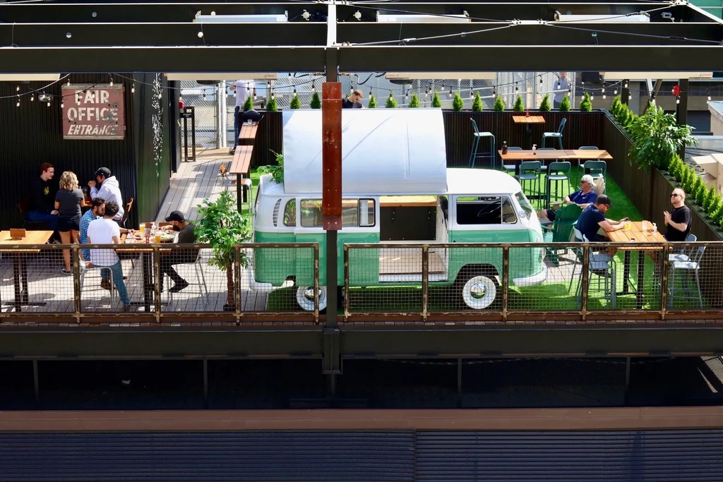Open-air rooftop bar with VW van counter, turf, and socializing patrons.