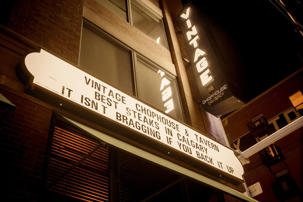 Illuminated Vintage Chophouse & Tavern sign on a brick building at night.