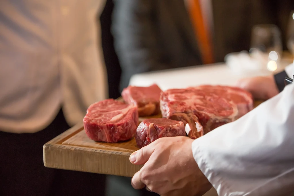Chef holding a wooden board with various raw marbled steaks.