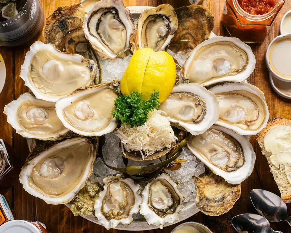 Many raw oysters on the half shell, served on ice with lemon.