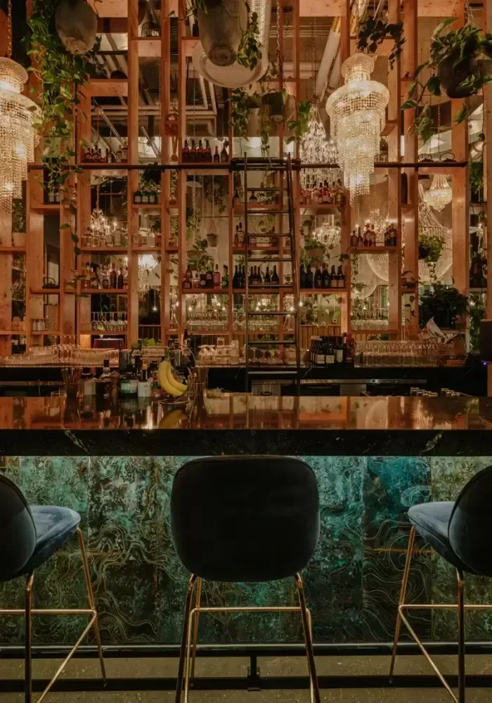 Stylish bar interior with turquoise patterned counter, velvet stools, and shelving.