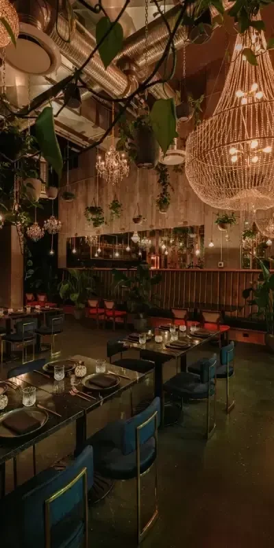 Luxurious restaurant interior with velvet chairs, ornate chandeliers, and lush plants.