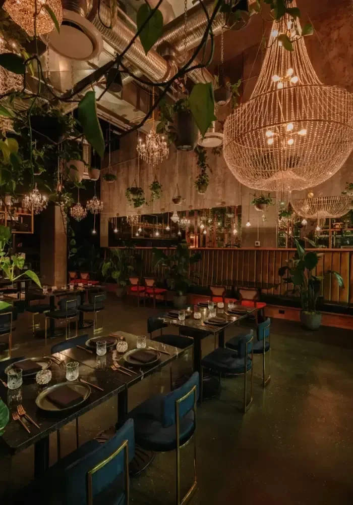 Luxurious restaurant interior with industrial ceiling, lush plants, ornate chandeliers.