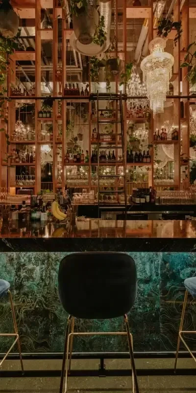 Bar with teal marble, plant-filled shelves, and crystal chandelier.