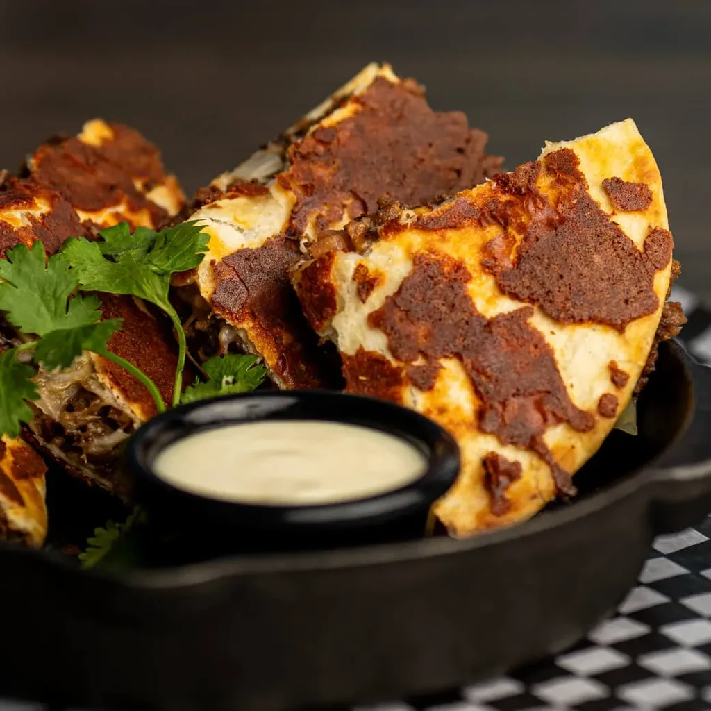 Golden-brown quesadilla slices in a skillet with creamy sauce and cilantro.