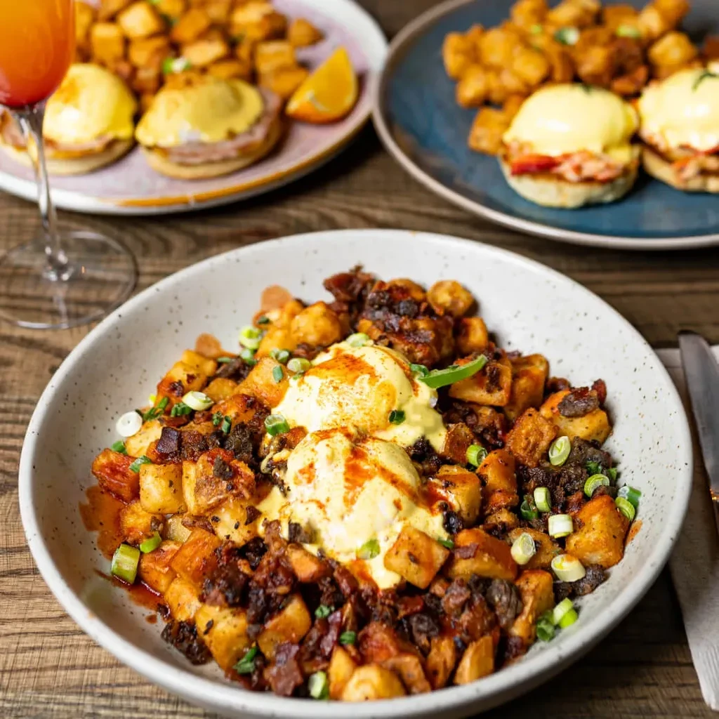 Large bowl of breakfast hash topped with poached eggs and hollandaise.