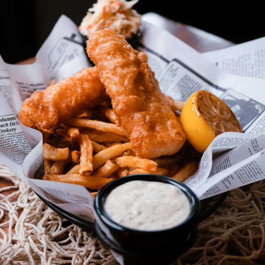 Golden-brown fish and chips in a basket, with lemon and sauce.