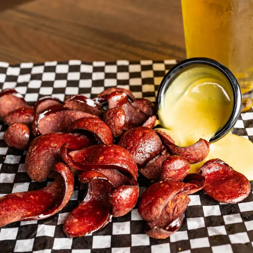Cooked sausage slices and spilled yellow sauce on checkered paper.