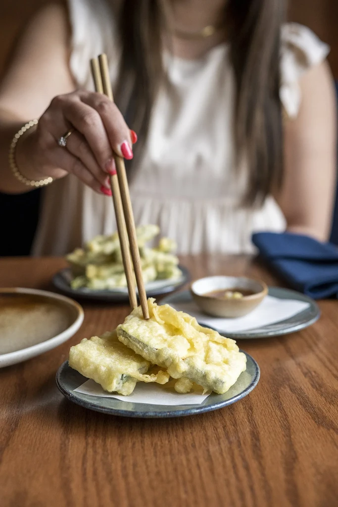 Hand with red nails uses chopsticks to pick fried tempura.