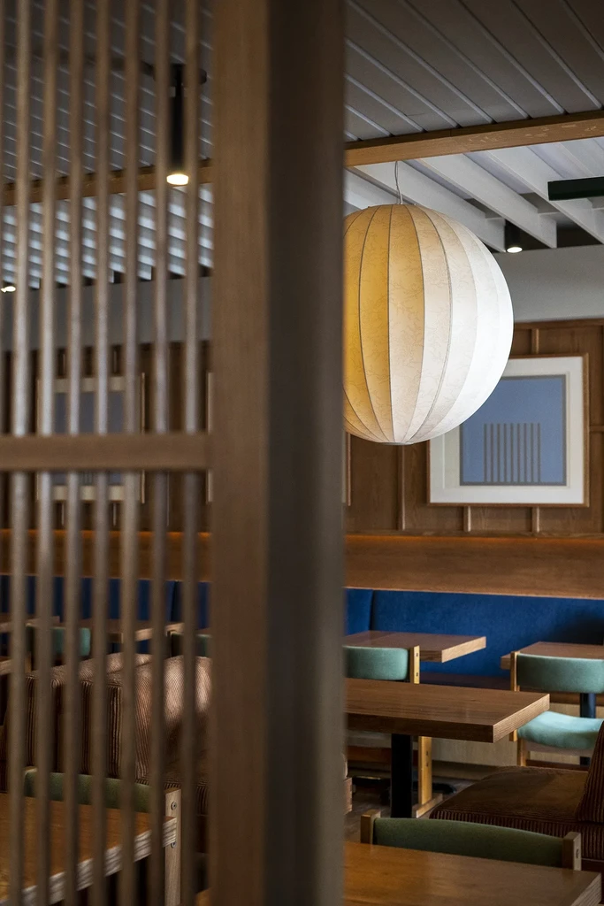 Modern restaurant interior with wooden screen, blue booth, and large paper lantern.