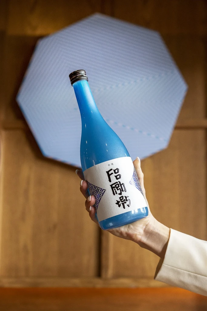 Hand holds a traditional sky-blue bottle with Japanese characters.