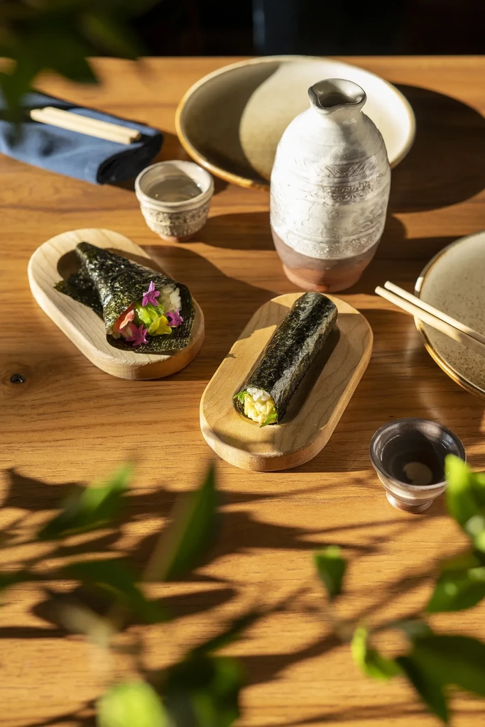 Two temaki rolls, one open, with sake bottle and chopsticks.