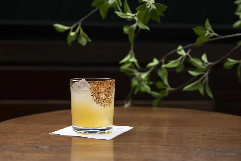 Cocktail in rocks glass with seasoned rim, ice, on coaster.