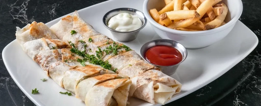 Segmented wraps with green herbs, french fries, ketchup, and white sauce.
