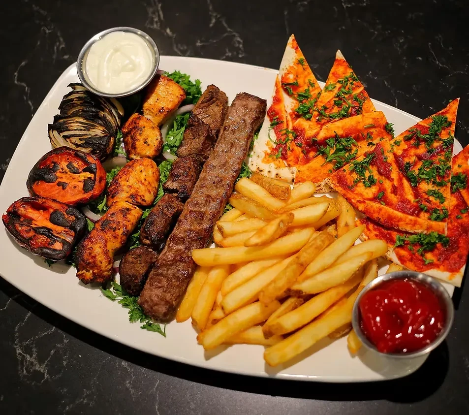 Grilled meat platter with chicken, kebab, fries, flatbread, and sauces.
