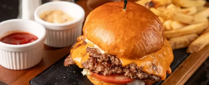 Gourmet burger with melted cheese, fries, and two dipping sauces.