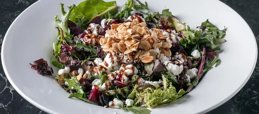 Salad with greens, crumbled cheese, beets, almonds, and balsamic drizzle.