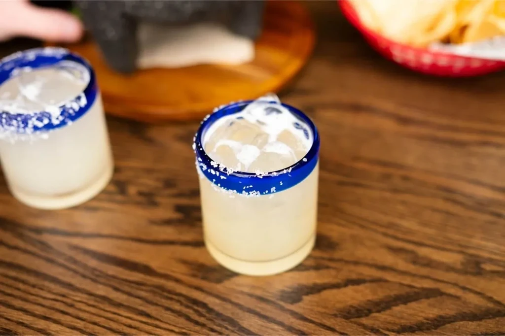 Two salt-rimmed margaritas with blue bands on a wooden table.