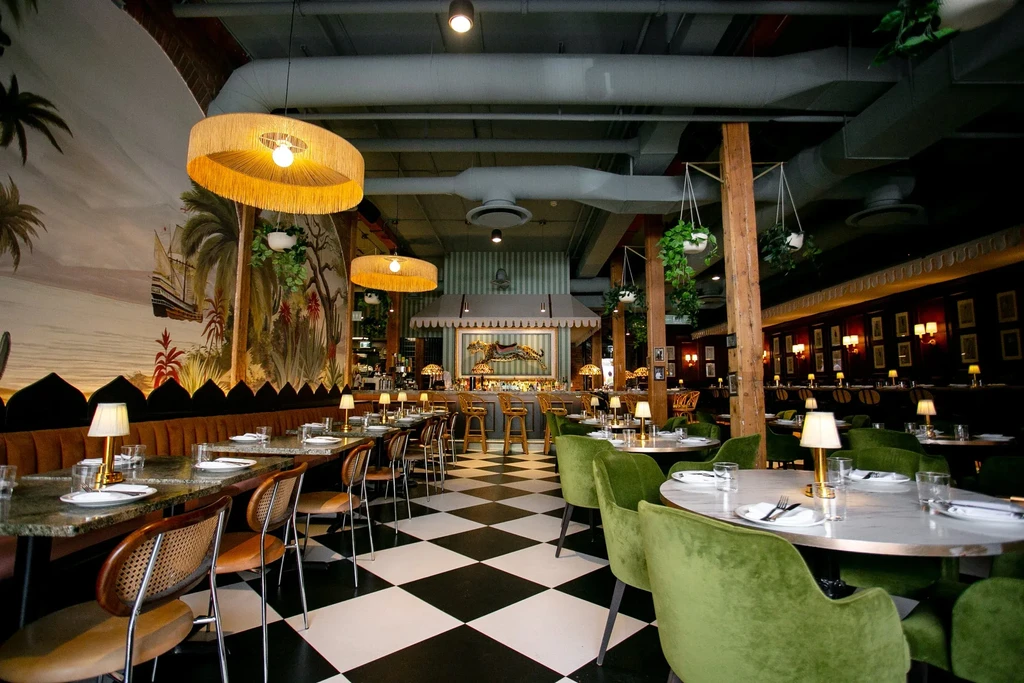 Empty, eclectic bar and restaurant interior with tropical mural and checkerboard floor.