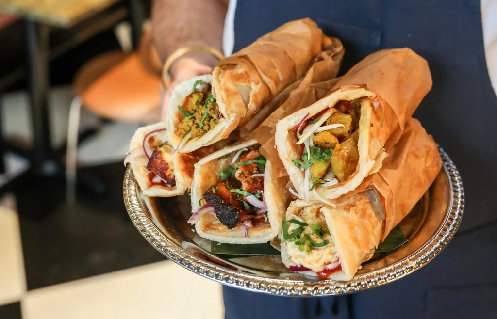 Close-up of a silver platter with six vibrant, partially unwrapped kathi rolls.