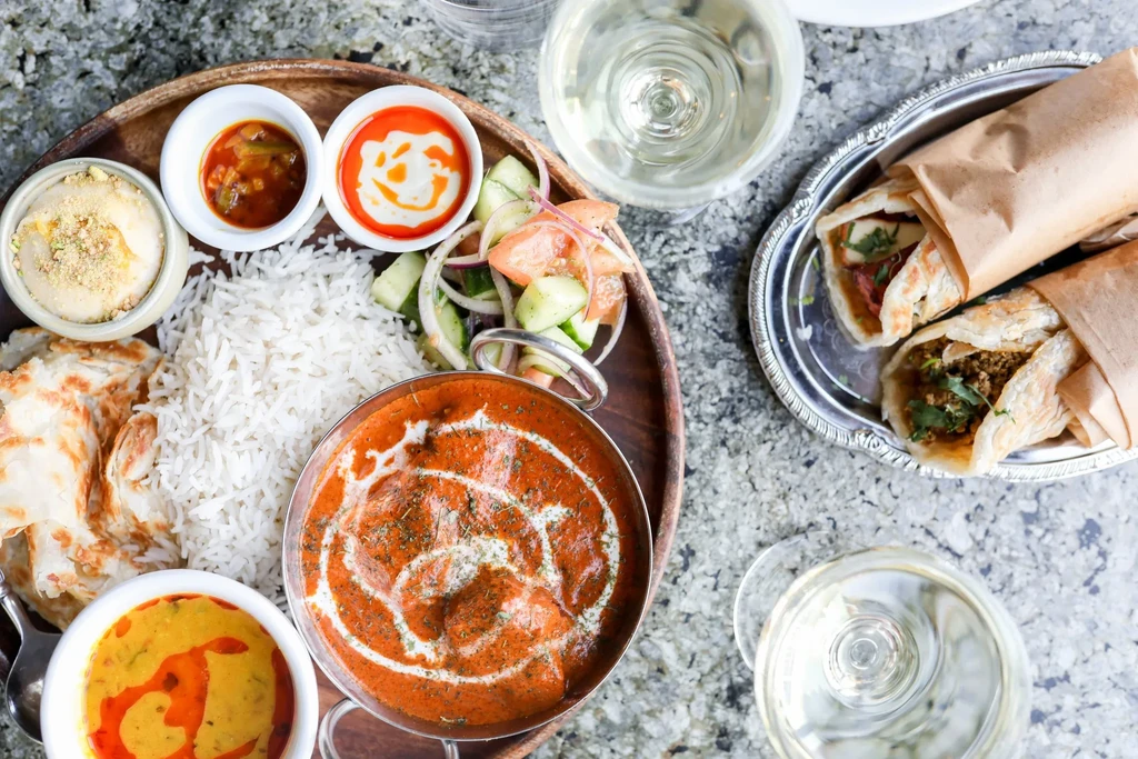 Overhead shot of a vibrant Indian thali, kathi rolls, and wine.
