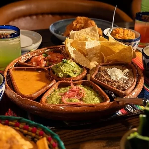 Tortilla chips and multiple Mexican dips on a wooden serving tray.