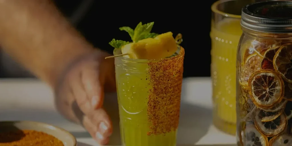 Green cocktail with chili-salt rim, pineapple, and mint garnish.
