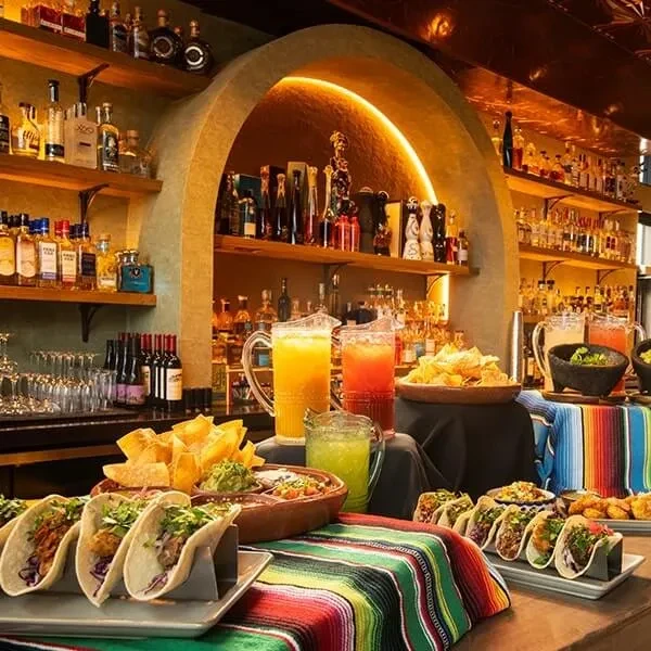 Vibrant Mexican bar displays tacos, chips, guacamole, and colorful drinks.