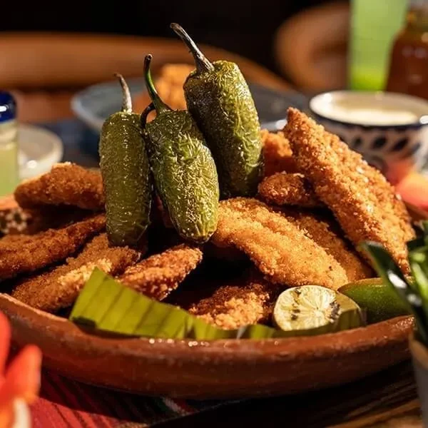 Rustic bowl of fried breaded food with chilies and lime.