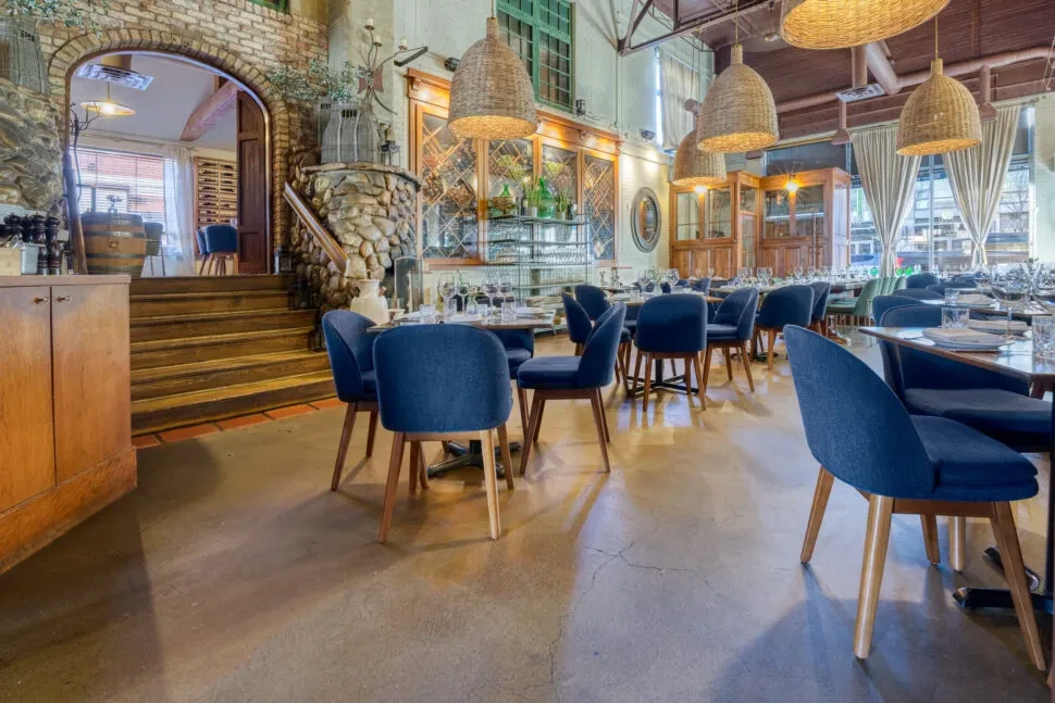 Empty upscale restaurant with brick arches, blue chairs, and rattan lights.