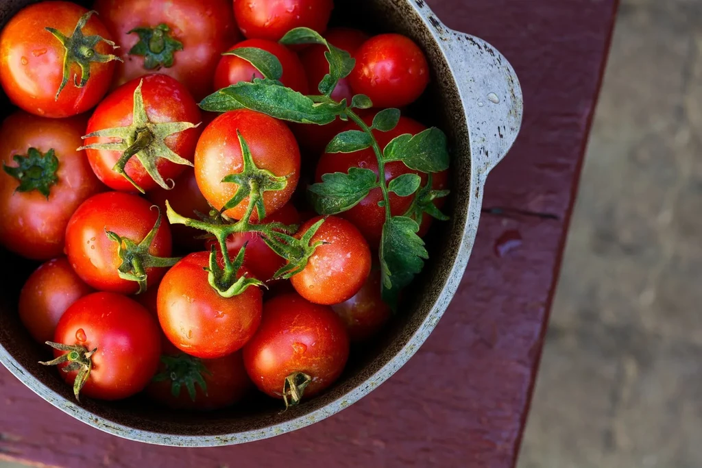 Fresh red tomatoes with green stems in a rustic bowl on wood.