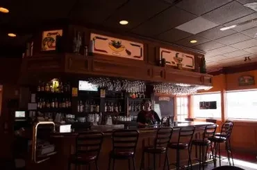 Stocked wooden bar with hanging glasses, bar stools, and a bartender.