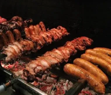 Sausages and ribs cooking on skewers over hot coals.
