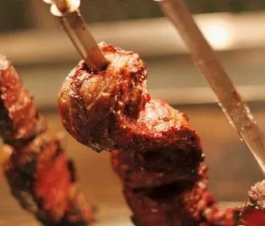 Glistening, charred, well-cooked roasted beef on metal skewers.