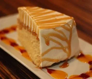 Cake slice with whipped cream, caramel, and fruit sauce on plate.