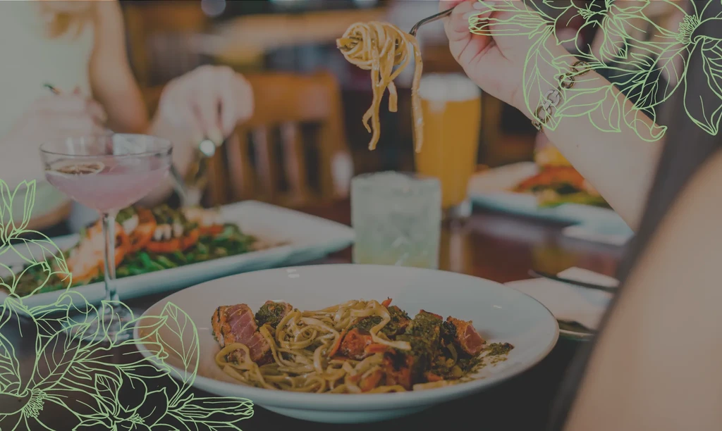 Hand twirls seared tuna pasta with green sauce at a restaurant table.