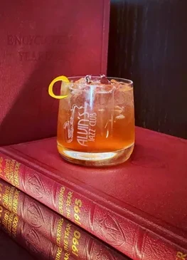 ALVIN'S Jazz Club cocktail with lemon twist rests on vintage books.