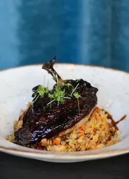 Glazed meat on pilaf with microgreens in a rustic white bowl.