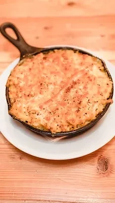 Golden-brown baked mac and cheese in a cast iron skillet on wood.