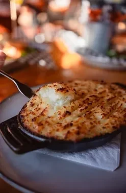 A fork scoops golden-brown gratin from a dark cast-iron skillet.