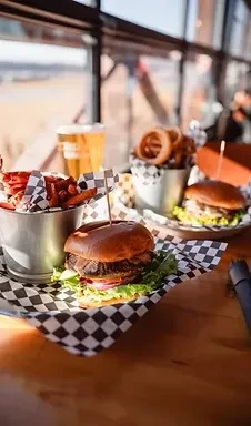 Burgers, sweet potato fries, onion rings, and beer on a wooden table.