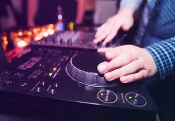 Hands operate a DJ controller amidst vibrant, blurred club lights.