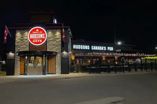 Illuminated Hudsons Canada's Pub building and patio at night.