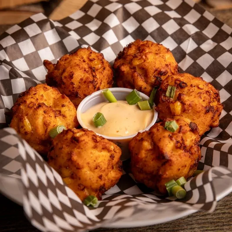 Six golden-brown fritters with orange dipping sauce and green onions.